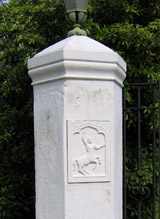 A Spanish Revival style driveway entry gate stucco column with Casa del Herrero logo and iron lantern mounted to the top.