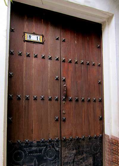 A historic pair of wood plank Spanish doors with iron work details and stamped metal lower panel. Photo taken in Seville, Spain.