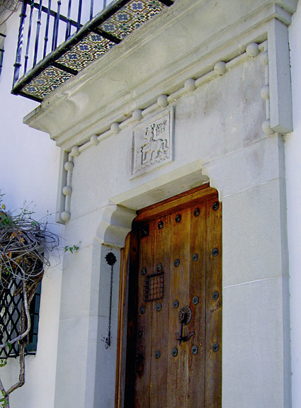 A cut stone front door surround at Casa del Herrero in Montecito, California. Logo of George F. Steedman iron worker carved in stone above Spanish wood door with antique clavos and iron door knocker.