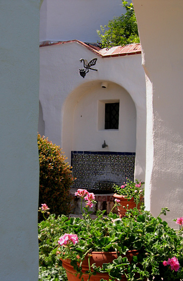 Spanish tiled wall fountain with basin, terra cotta pots with pink geraniums and courtyard at Casa del Herrero estate in Montecito, California