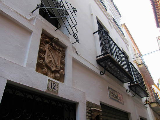 A carved stone family crest installed in a plaster wall above an iron door in Seville, Spain