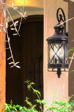 an affordable outdoor light for spanish style homes.  A rustic wood door with speakeasy iron grille in the background